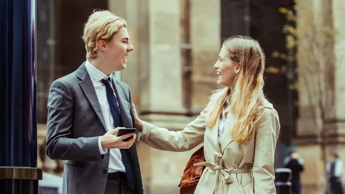 Businessman and businesswoman meeting up on the street to go to a meeting together.