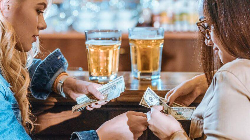 two girls with money paying for drink at bar.