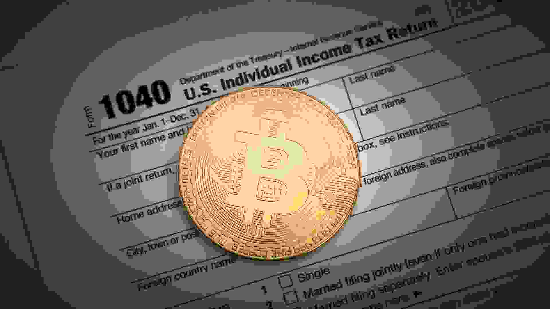 An editorial stock photo of a studio shot of a Bitcoin with some IRS 1040 tax forms.