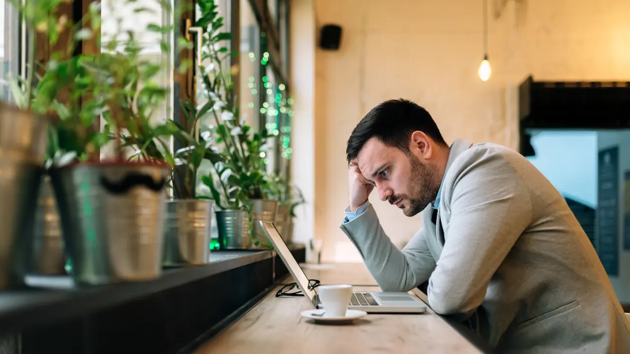 Worried man looking at laptop screen while sitting at modern cafe.