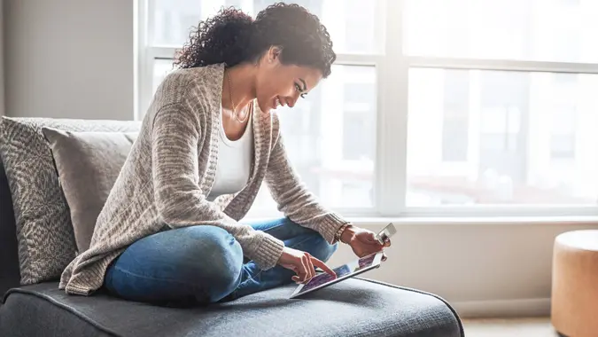cheerful young woman relaxing on a chair while doing online shopping on a digital tablet at home.