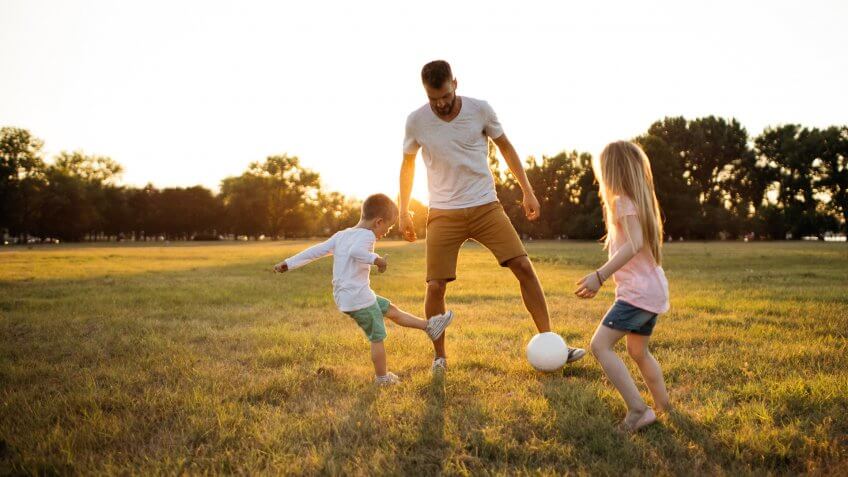 Kids and father playing soccer on a beautiful summer afternoon outdoors.