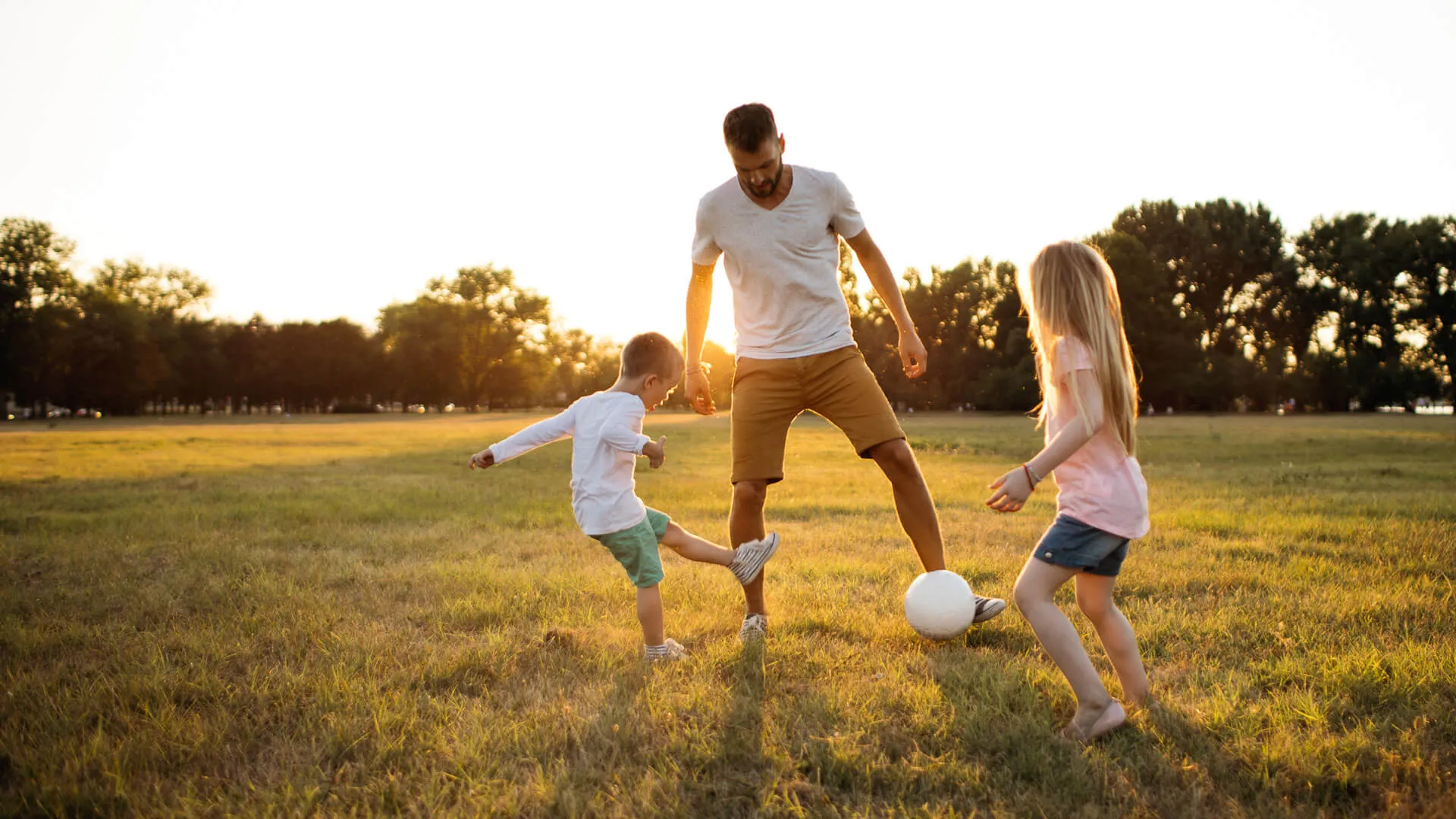 Kids and father playing soccer on a beautiful summer afternoon outdoors.
