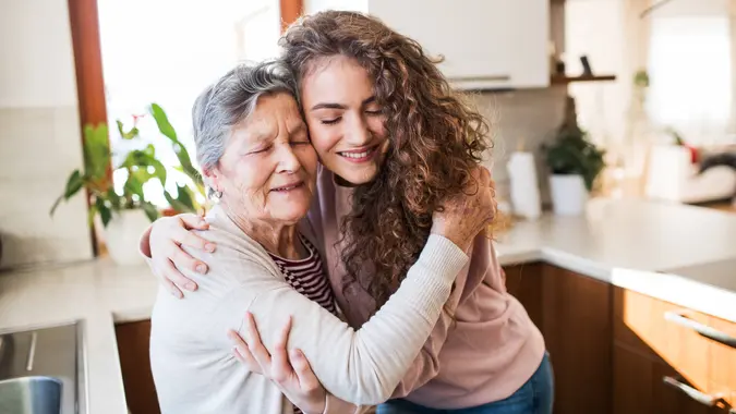 A teenage girl with grandmother at home, hugging.