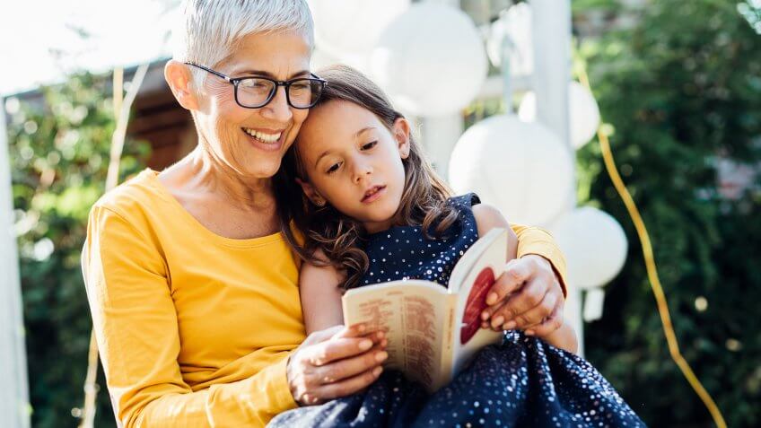 Old woman reading a book to her granddaughter when relaxing on a swing.