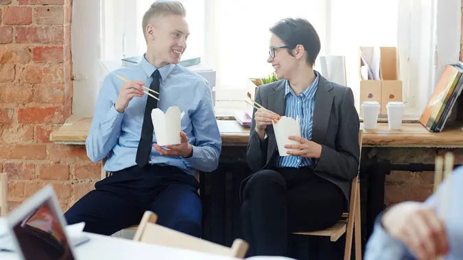 Happy office managers eating wok with chopsticks.