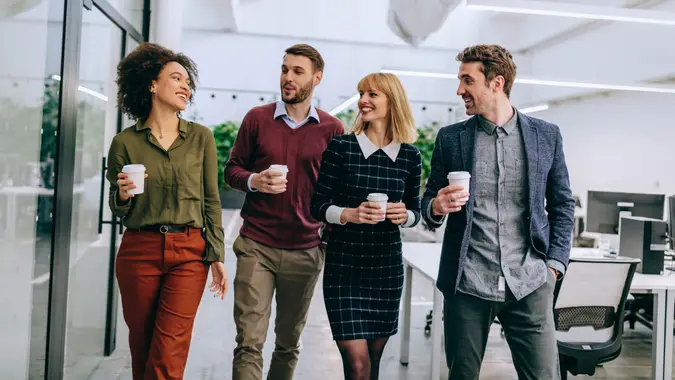 Group of diverse coworkers walking through a corridor in an office, holding paper cups.