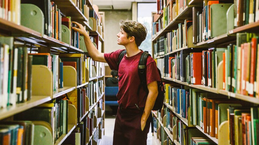 high school student in the library pulling out a book from the shelf