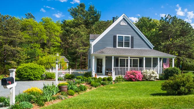 An American flag flies from the open porch and gardens surround a small  single family home on a Spring afternoon on Cape Cod on the Massachusetts coast.