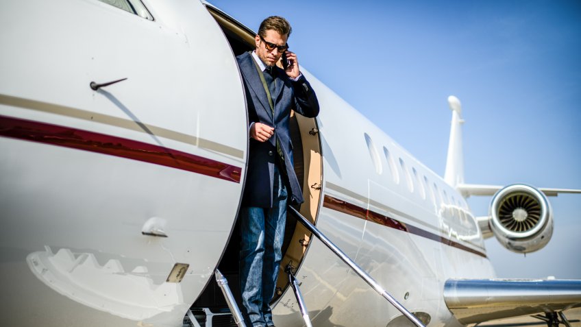 Man wearing elegant clothes exiting the private jet airplane and talking over mobile phone.