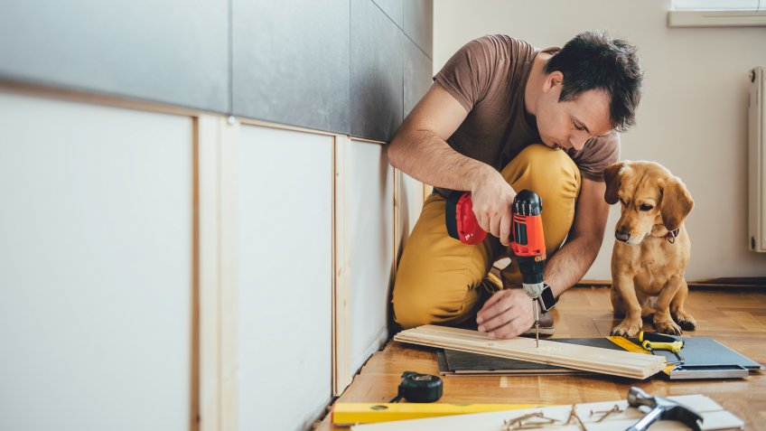 man using drill for home renovation project with dog