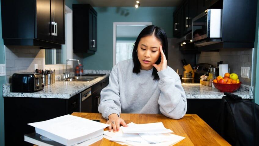 A female student worrying about financial issues at home in her apartment.