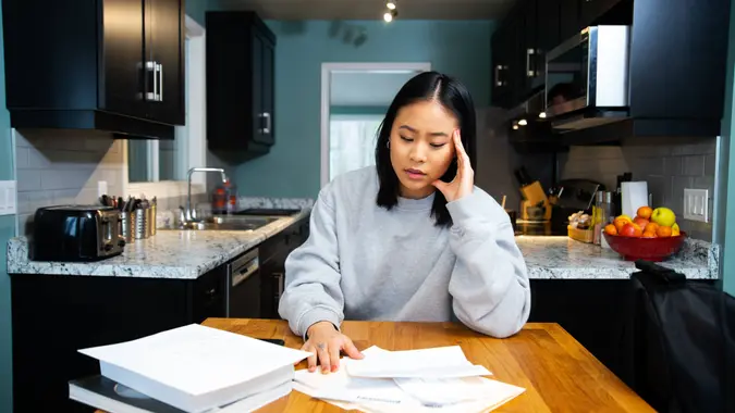 A female student worrying about financial issues at home in her apartment.