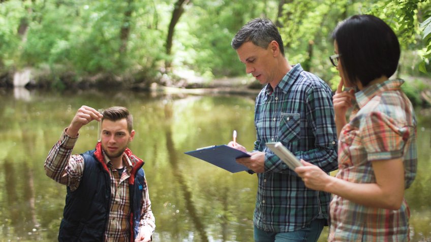 Three ecologists wearing casual clothing exploring lake and taking water sample.