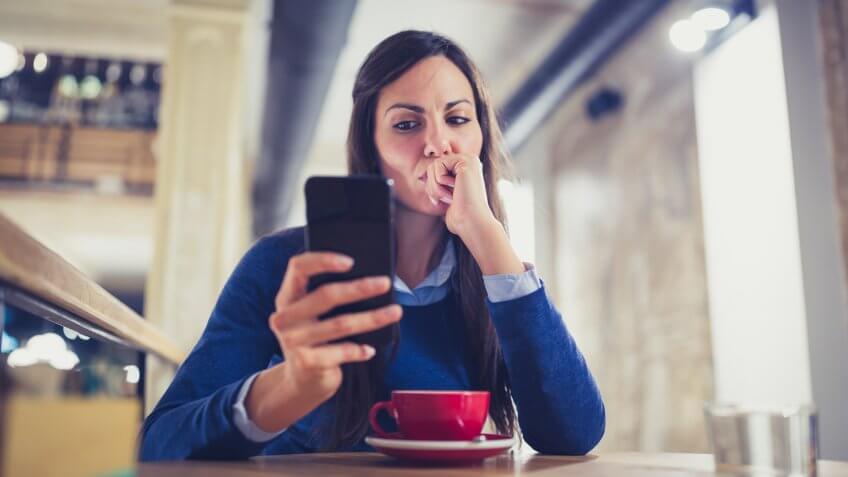 Young woman drink a cappuccino at the cafe, using mobile phone, texting.