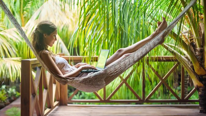 Young beautiful woman lying in a hammock with laptop in a tropical resort.