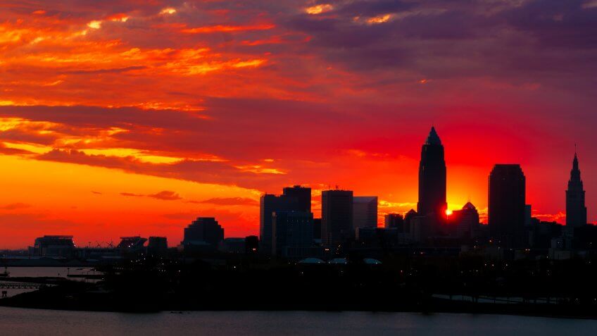 The rising sun peeks out from behind nearly silhouetted buildings of downtown Cleveland Ohio.