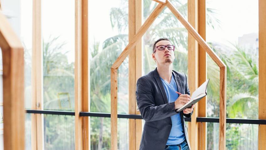 young engineer looking at a empty frames in a villa with tropical garden and writing something at his copybook.