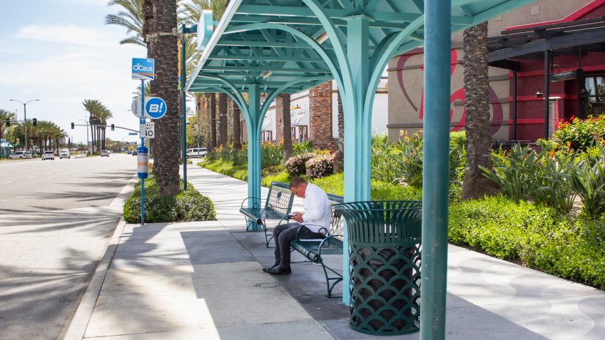 Garden Grove, California/United States - 04/01/19: A man sits at a covered bus stop near the street.
