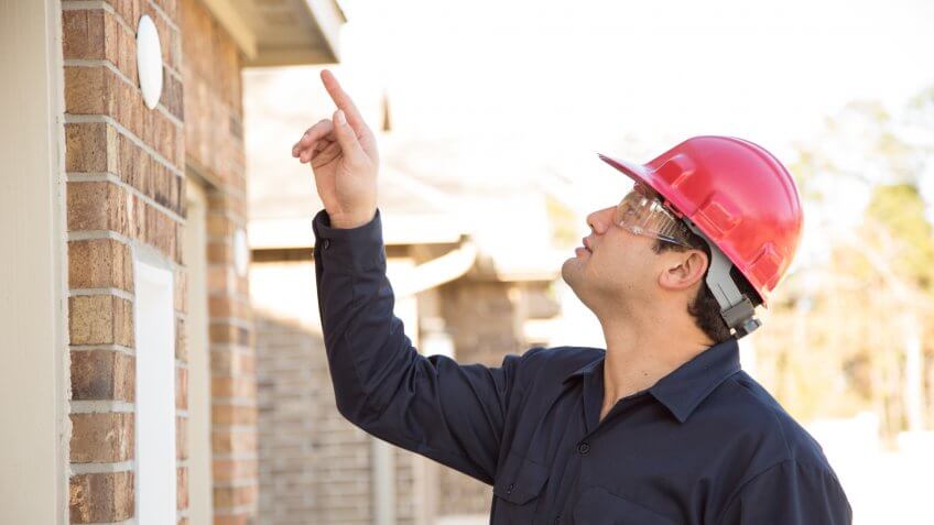 Latin descent home inspector, engineer, insurance adjuster, exterminator, or repairman examines recent house construction using his digital tablet.