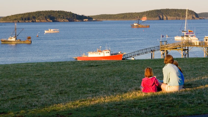 "Family watches harbor scenes as suns sets in Bar Harbor, Maine.