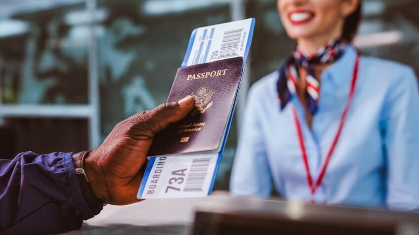 African American man holding boarding pass and passport at airline check-in desk at international airport.