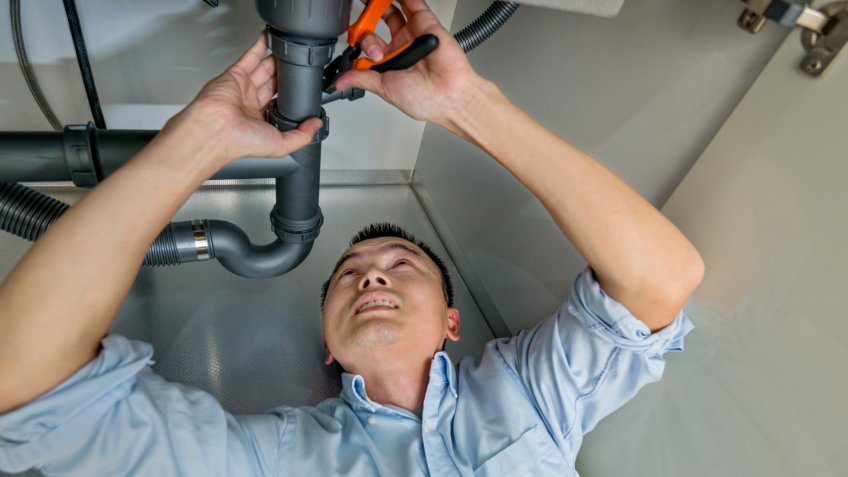 Man repairing sink pipe in the kitchen.