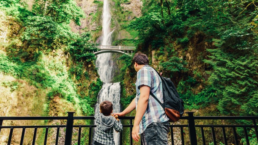 Father and his small son looking on Multnomah Falls waterfall along the Columbia River Gorge, Oregon, USA.