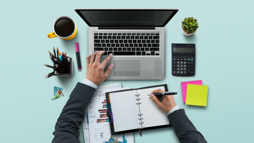 Office workplace with laptop, notebook, hand, office supplies, on turquoise background.