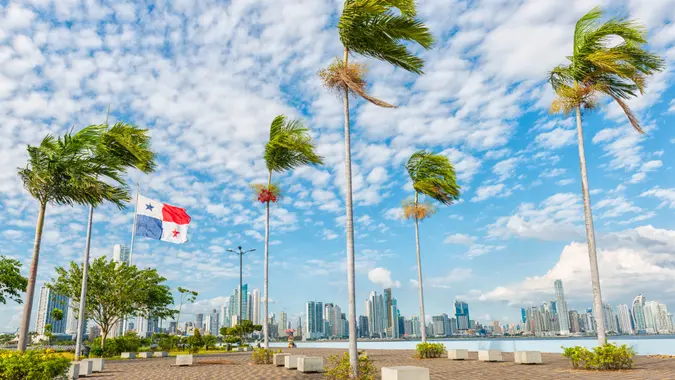 Panorama Panama city, in front palm trees and Panamian flag on plato, in background high buildings against blue sky.