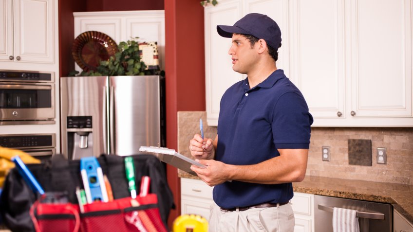 Hispanic repairman or blue collar/service industry worker makes service/house call inside customer's home kitchen.