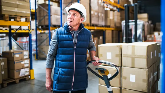 Senior male warehouse worker pulling a pallet truck with boxes.