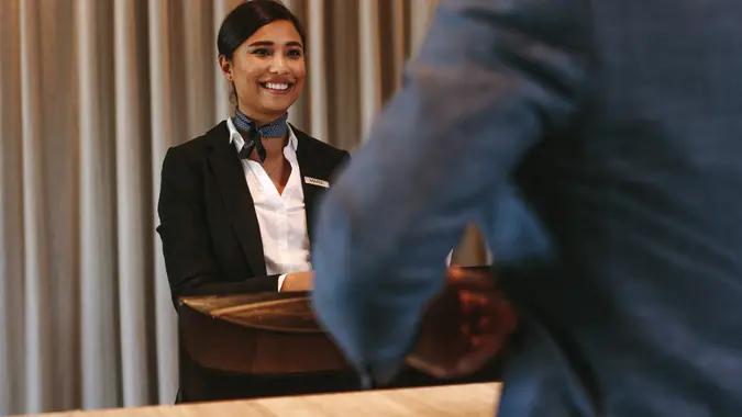 Smiling hotel receptionist talking with male guest at reception counter.