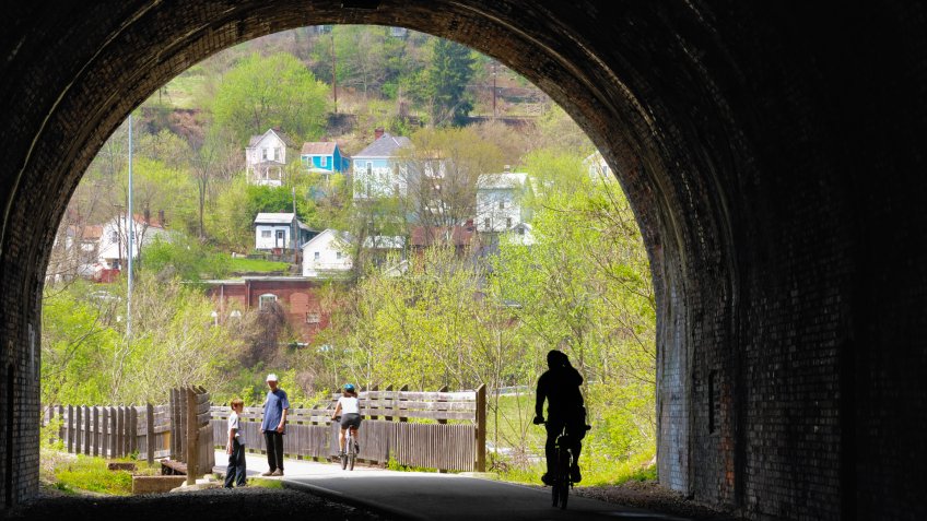 Wheeling, WV, USA - April 26, 2009: An elderly man and a boy stand at the entrance to a tunnel as bicyclists ride by on a walking and biking path that was converted from an old railroad line.
