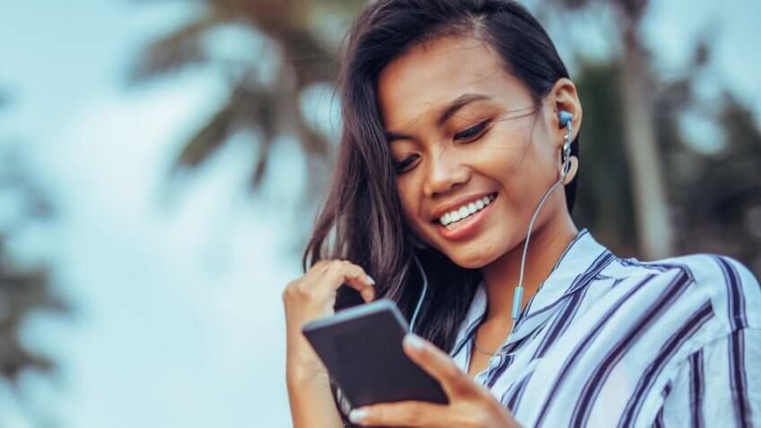Young woman with phone and earphones at the beach.