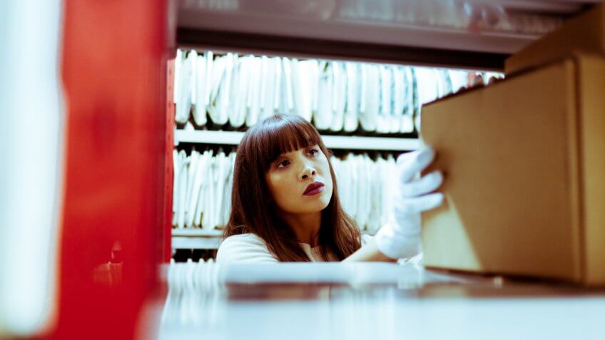 A woman handling files from the Hulton Archives, wearing white gloves.