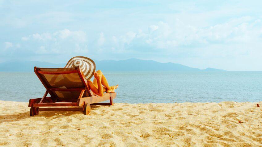 woman sunbathing in beach chair with outstretched arms on the beach.