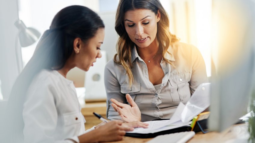 Shot of two young businesswomen talking to each other while being seated in the office at work.