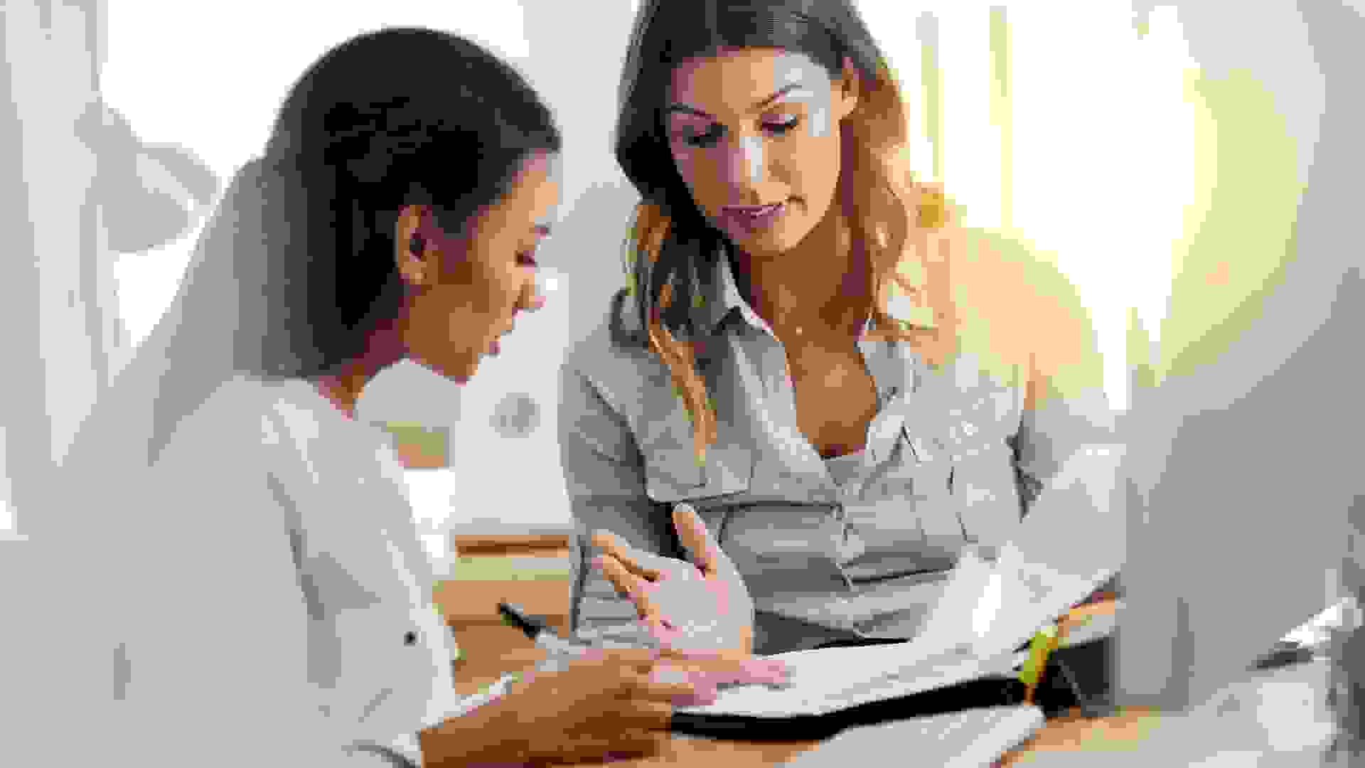 Shot of two young businesswomen talking to each other while being seated in the office at work.
