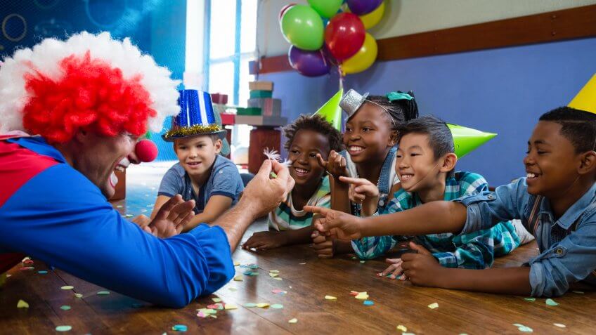 Clown showing feather to children sitting at desk during birthday.