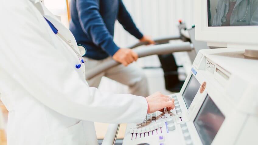 Senior patient is being measured by a doctor for a stress test on a treadmill.