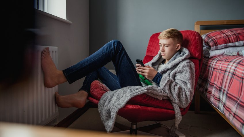 A teenage boy uses his phone and relaxes in his bedroom.