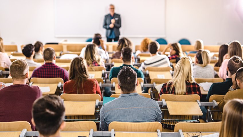 Back view of large group of students paying attention on a class at lecture hall.