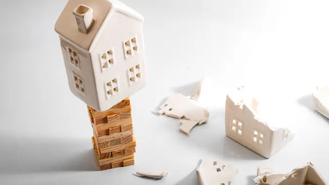 Financial risk, unstable real estate investment and shaky housing market concept with a home on stacked wooden building blocks surrounded by the ruins and debris of another house that collapsed.