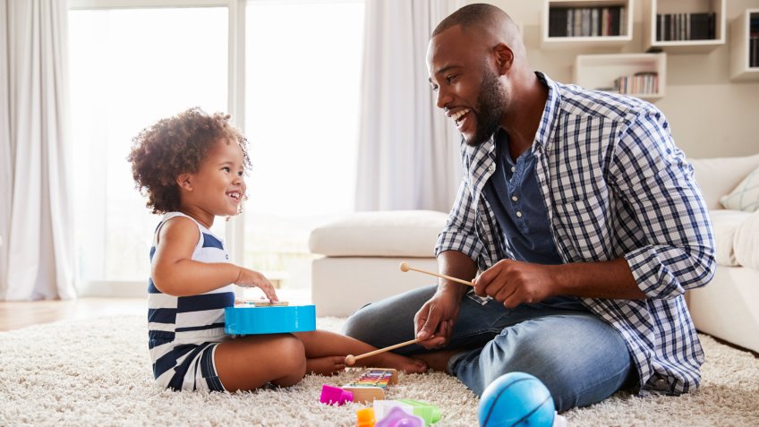 Young black father playing with daughter in the sitting room.