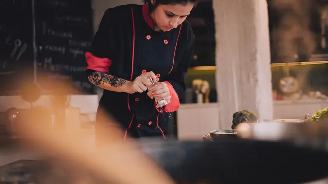 Portrait of a young tattooed chef, doing magic in her kitchen.
