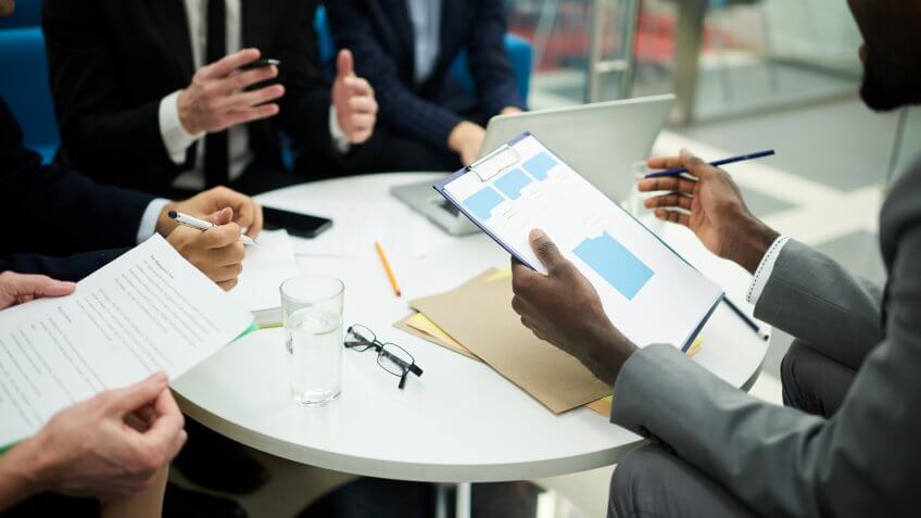 Mid section crop of unrecognizable business people meeting in office, focus on African man holding clipboard, copy space.