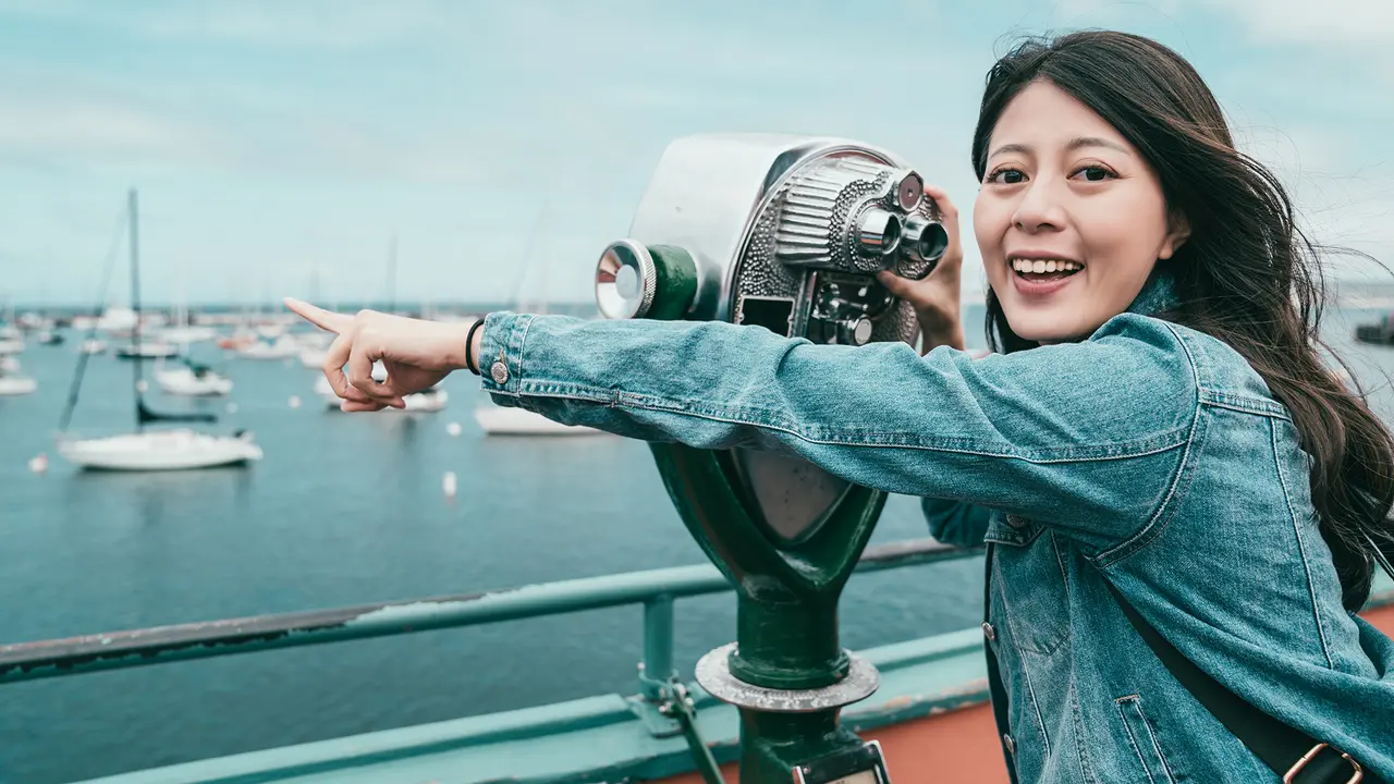 happy beautiful girl pointing at sea while looking through a telescope for finding interesting stuff.