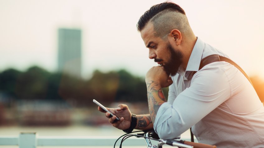 Businessman pushing his city bicycle and using his smart phone.