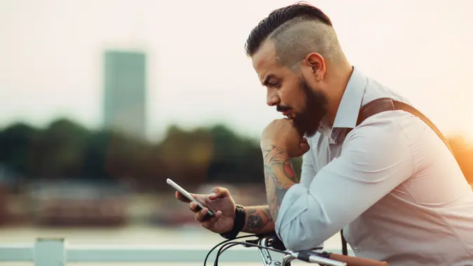Businessman pushing his city bicycle and using his smart phone.